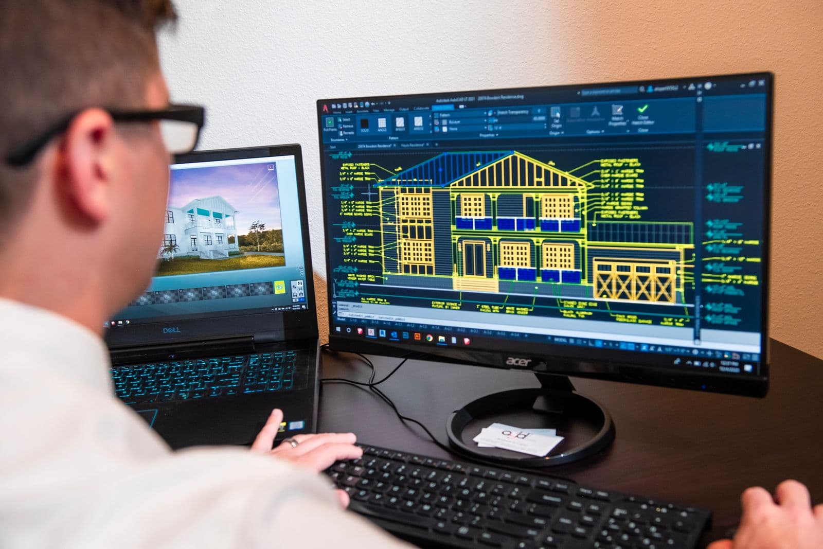 AutoCAD architectural elevation drawing on monitor + 3D house render on laptop