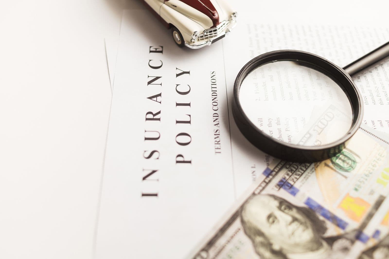 'Insurance Policy' document with magnifying glass and toy car (compare/examine insurance concept)