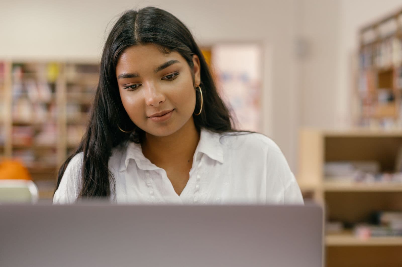 Young Indian student focused on a laptop in a study/library setting (Indian context for an India-based EdTech)