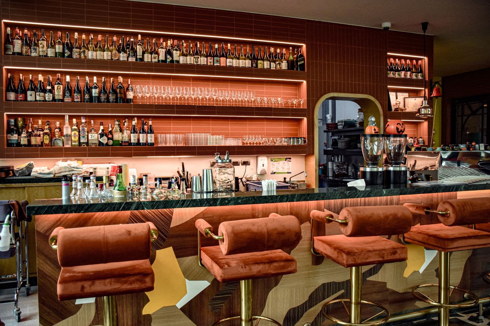 Warm upscale restobar interior - backlit bottle shelf, marble counter, plush stools (no faces/brand/signage)
